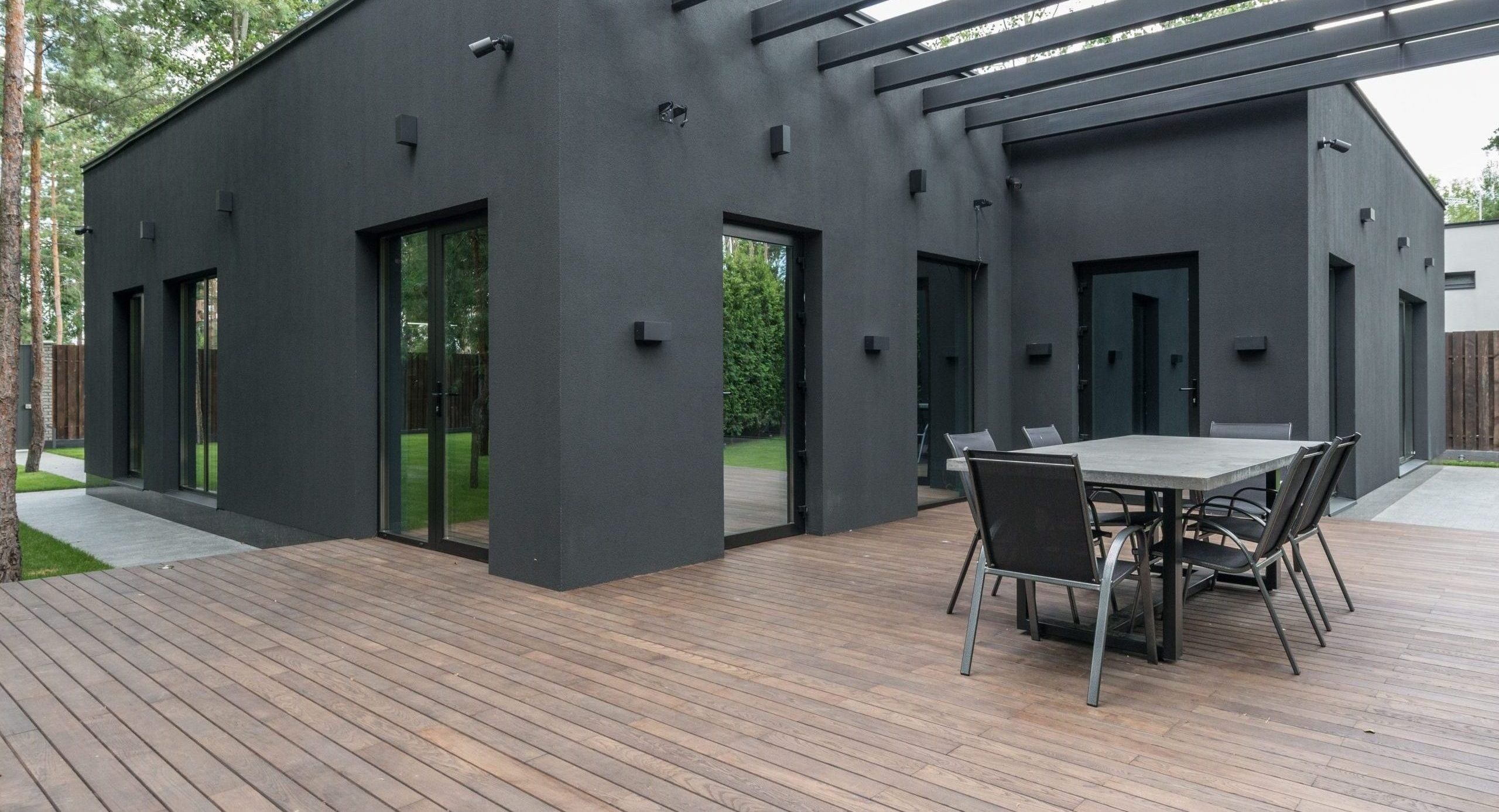 Contemporary black house with spacious wooden terrace and outdoor seating area.